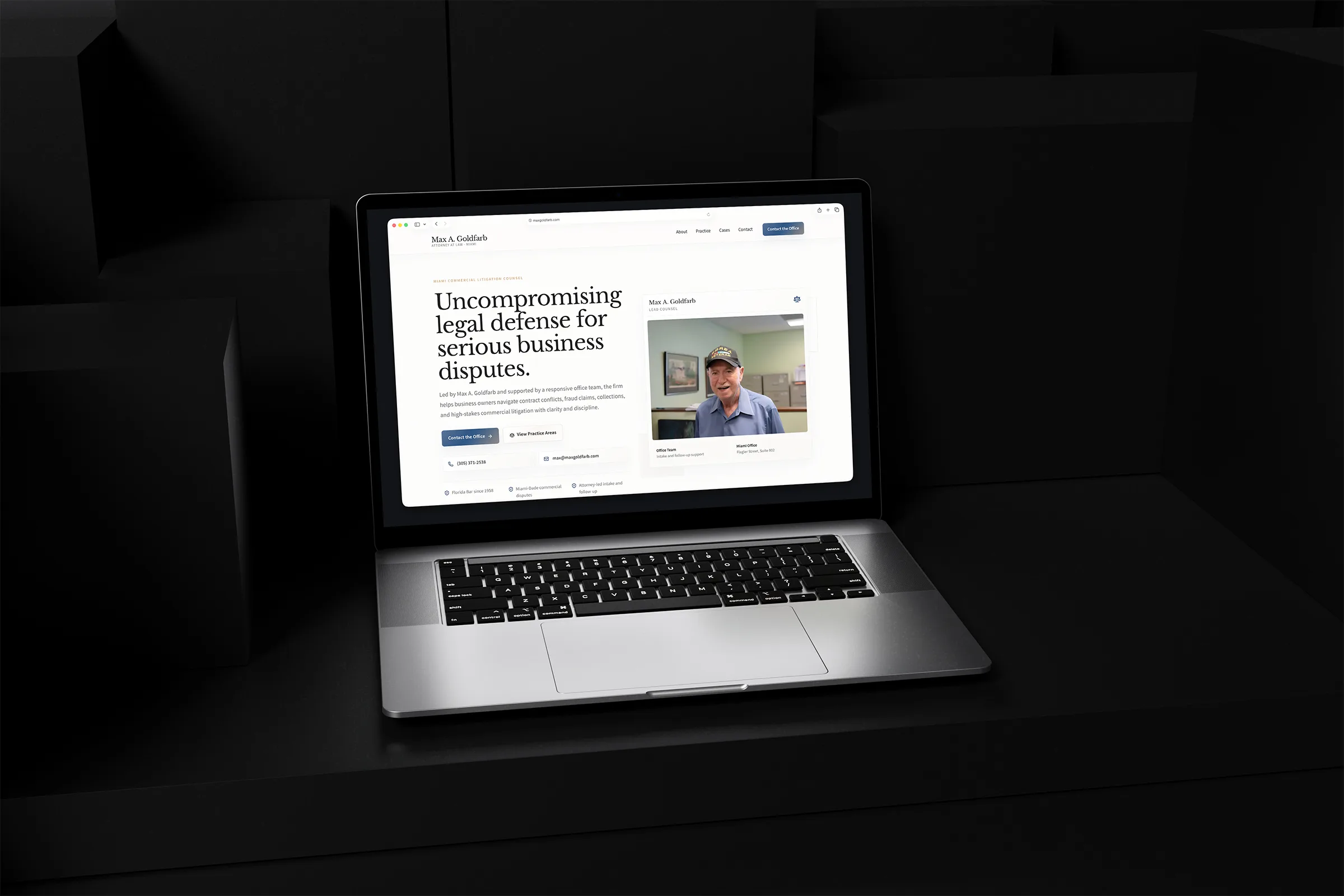 Max Goldfarb law firm website displayed on a laptop in a dark geometric setting.